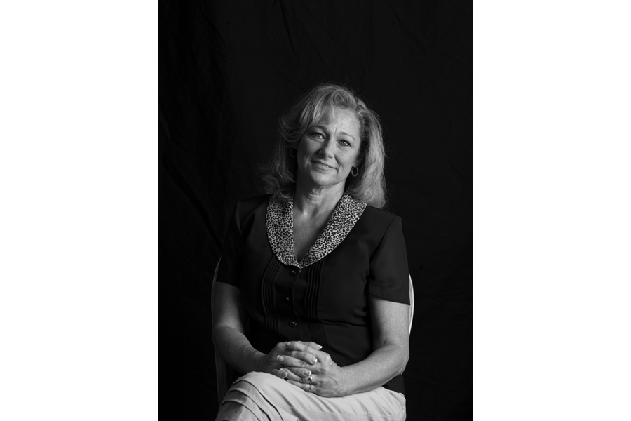 This is a Brian Charles Steel black and white photographic portrait of Allison.  She is positioned toward the center, and lit with a Rembrandt style.  The main light source is coming from the right.  She is shown from the waist up, and she looks directly into the camera.  Allison has shoulder length blond straight blond hair.  She is holding her hands together over her stomach.  Allison is wearing a short-sleeved button up shirt. 