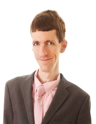 This is a photographic portrait of photographer Brian Charles Steel.  Steel has congenital fiber type disproportion, which causes him to be thin and small framed.  Steel is positioned on the right side of the frame and he fills it from top to bottom on that side.  You see him from just above the waist.  He is wearing a suit with a long sleeved dress shirt with dress slacks.